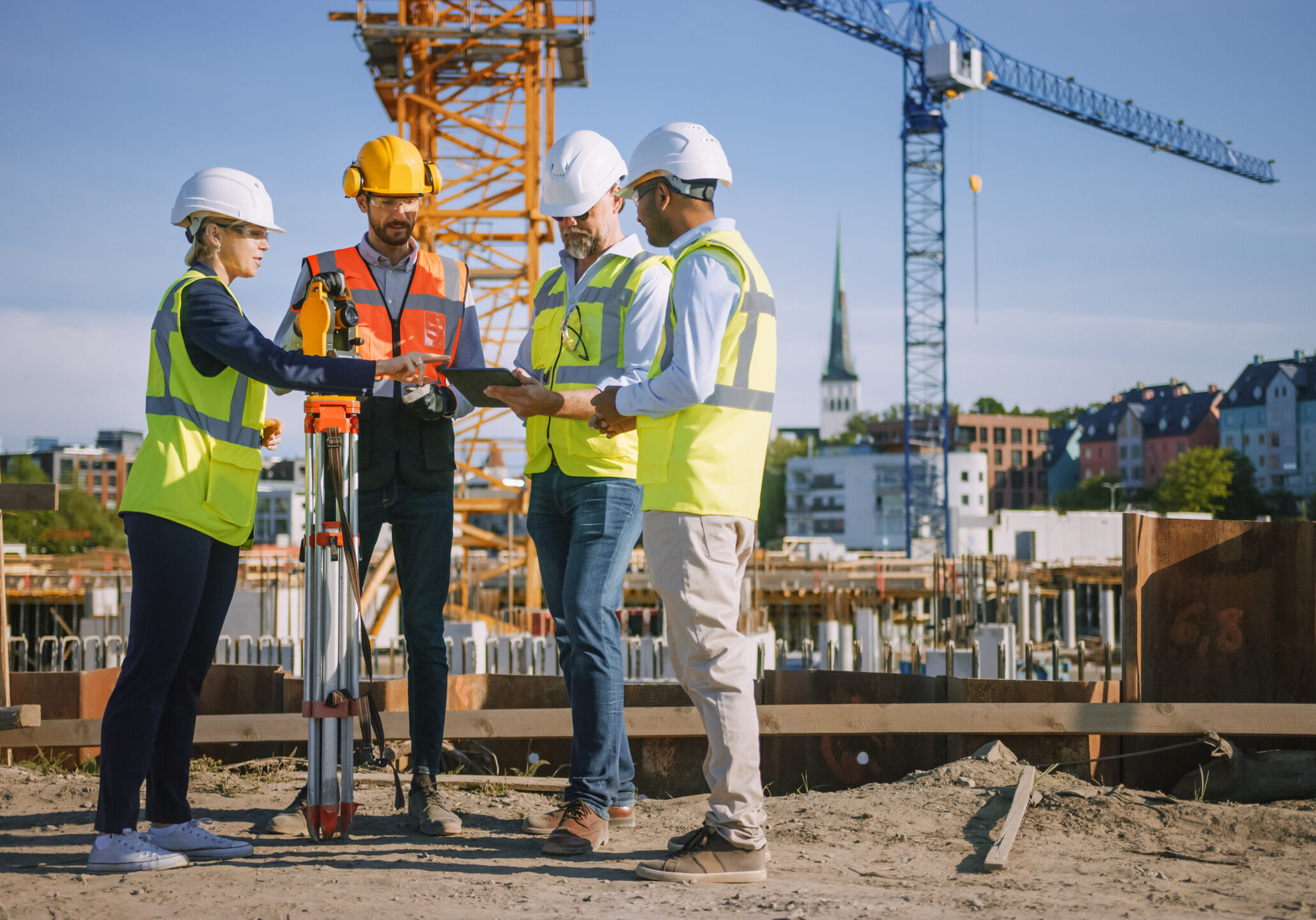 Diverse Team of Specialists Use Tablet Computer on Construction Site. Real Estate Building Project with Civil Engineer, Architect, Business Investor and Surveyor with Theodolite Discussing Plans.
